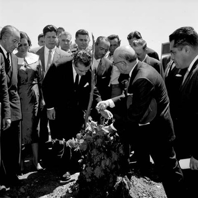 Adolfo López Mateos acompañado del gobernador y funcionarios públicos tocando una planta de uva en un viñedo