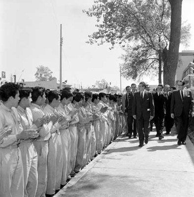 Adolfo López Mateos, José Alvares Amézquita y miembros de su comitiva son recibidos por una valla de individuos, durante una inauguración