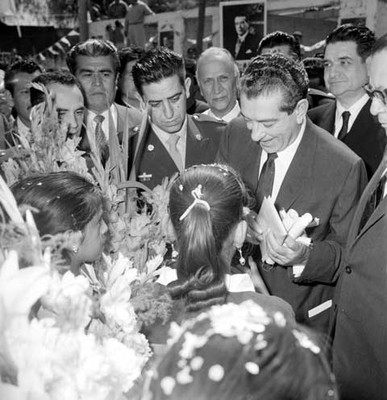 Adolfo López Mateos acompañado de Ernesto P. Uruchurtu recibiendo obsequios y adornos florales por parte de unas niñas