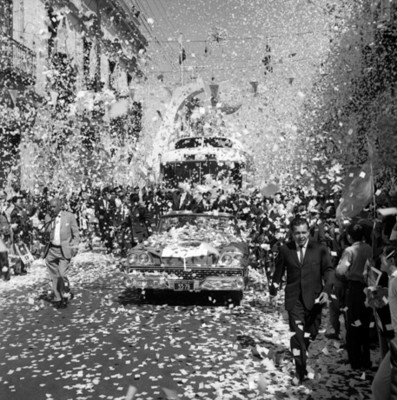 Adolfo López Mateos en un automóvil presidencial es ovacionado por la gente en su recorrido por las calles de Puebla