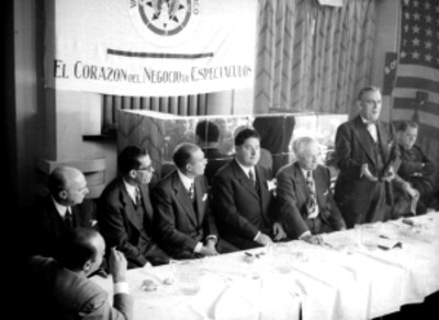 Empresarios cinematográficos escuchando las palabras de un individuo durante la inauguración del Variety Club