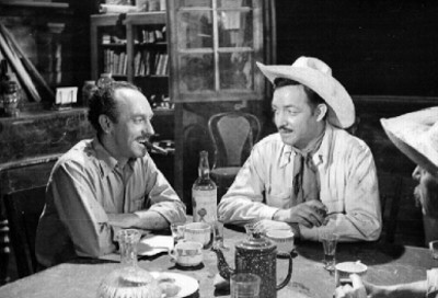 Jorge Negrete conversando con otro actor en una mesa, durante filmación de escena