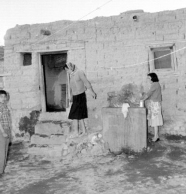Mujeres haciendo trabajos domésticos frente a una casa rústica habitada por militares