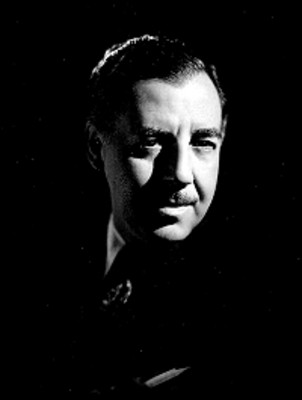 Fernando Soler, actor, sentado de perfil en una silla, viste de traje y corbata, retrato