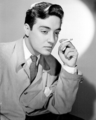 Armando Saenz, actor, viste de traje y corbata con cigarrillo en mano cerca de su rostro, retrato