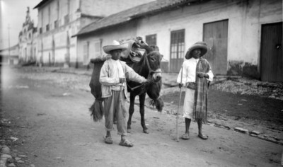 Arrieros junto a burro con carga de carbón en la calle de un poblado