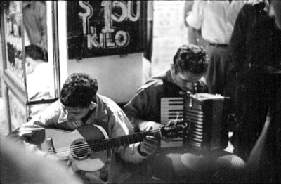 Músico callejero toca guitarra y acordeón en una banqueta