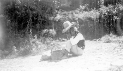 Hombre con sombrero y canasta sentado al lado de un camino