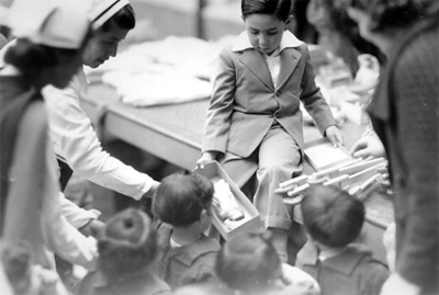 Niño de aproximadamente 5 años con traje, regalando juguetes a los niños de la casa, retrato