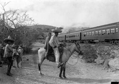 Pareja de hombre y mujer montados a caballo frente al ferrocarril