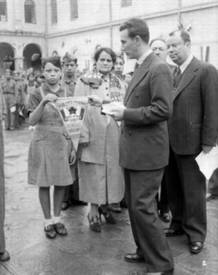 Ramón Beteta entregando un banderín a una estudiante en presencia de Rubén Romero y demás personalidades