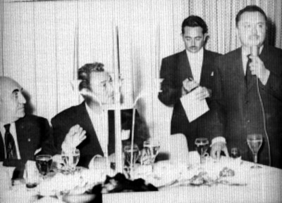 Orador y empresarios cinematográficos presidiendo una ceremonia en un salón