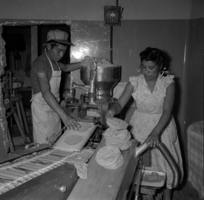 Hombre y mujer haciendo tortillas en una máquina de cinta metálica