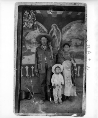 Familia de pie, frente a una imagen de la Virgen de Guadalupe