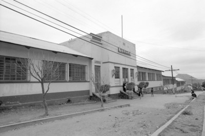 Gente en calle frente a escuela, vista lateral