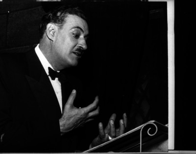 Salvador Novo, escritor leyendo un documento durante un acto en un salón