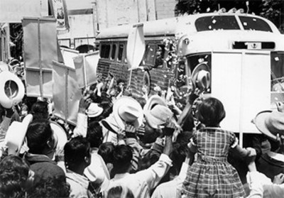 El presidente Díaz Ordaz saluda cordialmente a la multitud que esperaba su llegada en las calles de esa población, él se asoma por la ventana del bus
