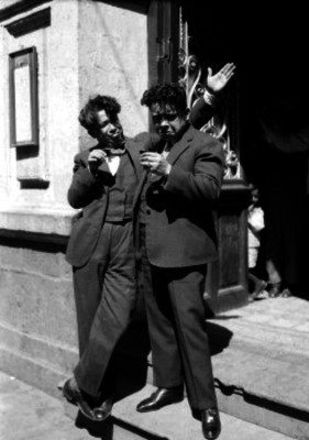 Joaquín Pardavé Arce bebiendo con otro actor frente a un edificio durante la filmación de una película