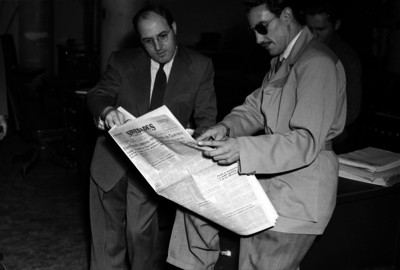 Ricardo del Río leyendo el periódico con un hombre, en una oficina