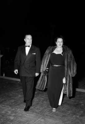 Antonio Ruiz Galindo y esposa vestidos elegantemente, caminado en un salón; durante un evento social.