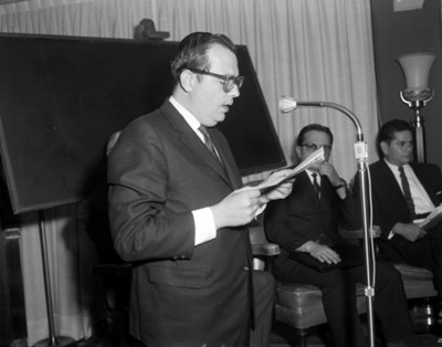 Ejecutivo de pie frente a microfono lee discurso en una asamblea
