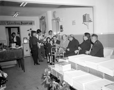 Sacerdote junto a hombres y niños escucha a un trío músical en la sala de espera