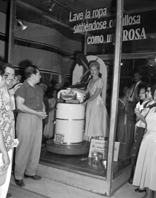 Hombres y mujeres observan a una modelo junto a una lavadora en un mostrador