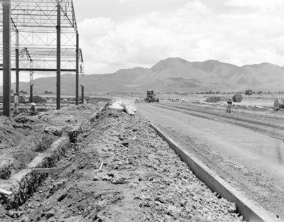 Hombres en carretera junto a armazón metálico de nave industrial en construcción