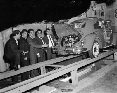 Hombres muestran motor de automóvil en planta automotríz, retrato de grupo