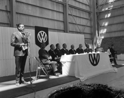 Hombre de pie frente a mocrófono durante reunión en la planta automotríz Volkswagen