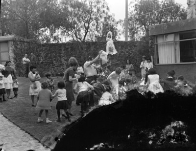 Hombre vacea dulces de una piñata a niños durante cumpleaños, en el patio de una casa