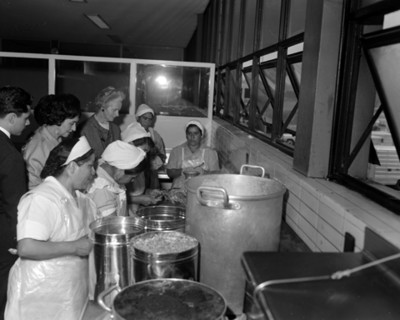 Eva Sámano de López Mateos y mujeres observan a cocineras preparar comida en el INPI.