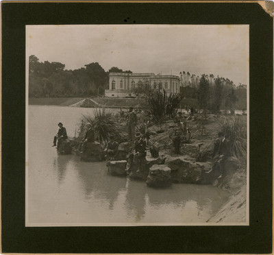 Hombres sentados junto al lago mayor y al fondo el Club del automóvil