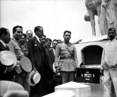 Hombre y oficial sostienen los restos de Emiliano Zapata ante su monumento