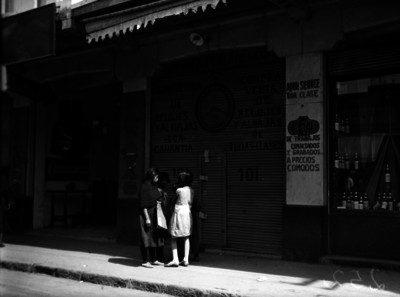 Mujer y niñas conversan frente a la joyería "La Perla" marcada con el N° 101